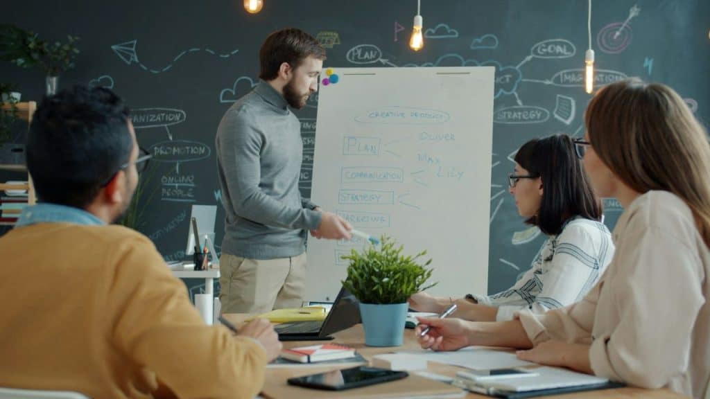 Man giving a presentation to three colleagues using a flip chart in a meeting room.