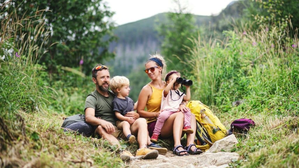 Family of four resting on a dirt trail, with one child looking through binoculars.