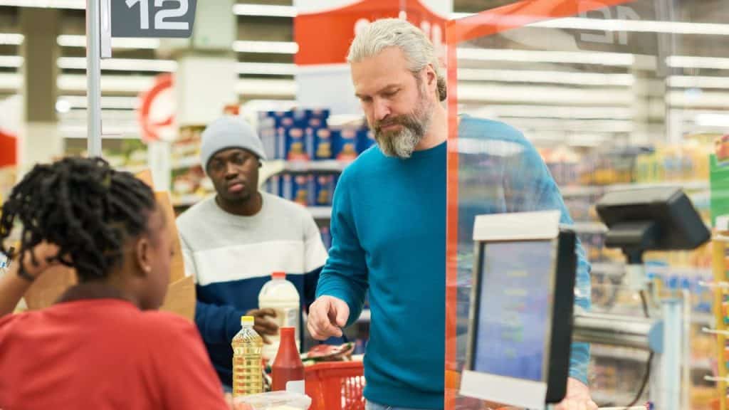 Older man with a beard in a blue sweater checking out groceries at a supermarket.