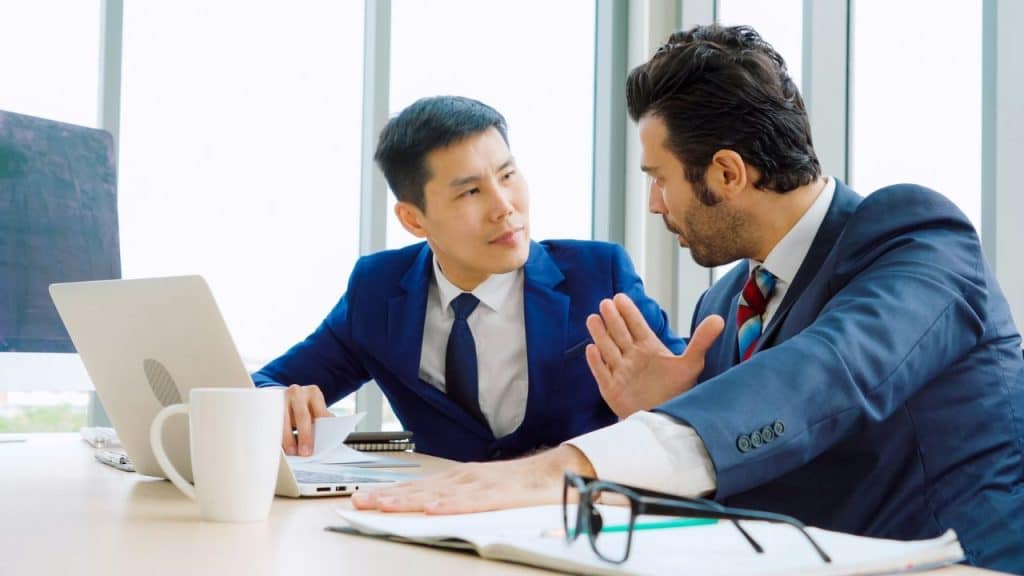 Two businessmen in suits having an intense conversation over a laptop in an office.