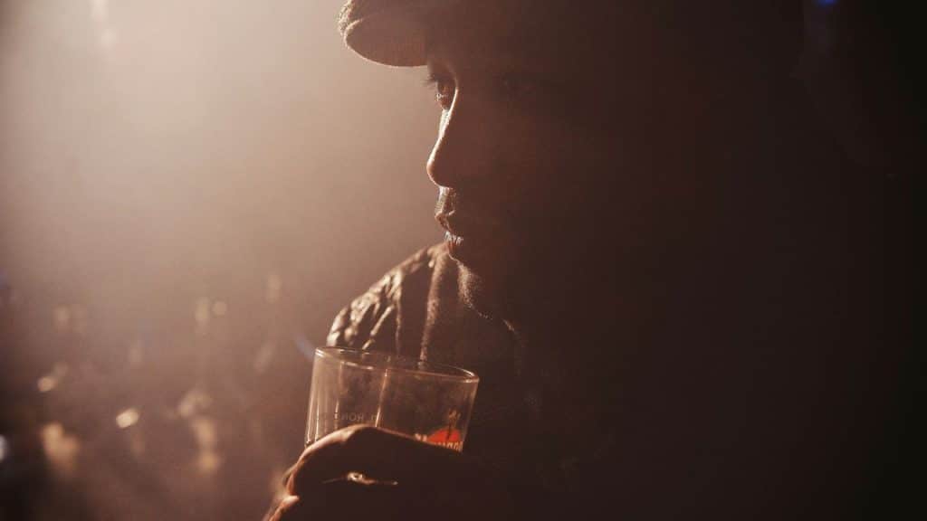 Close-up profile of a man in a hat holding a glass in a dimly lit space.