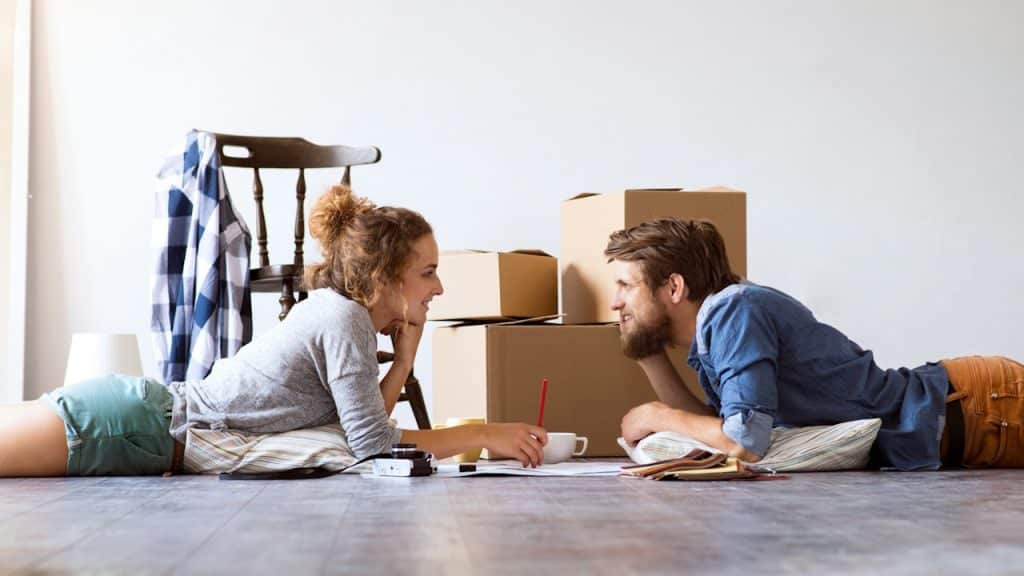 A couple moving into a new house and lying on the floor near cardboard boxes.