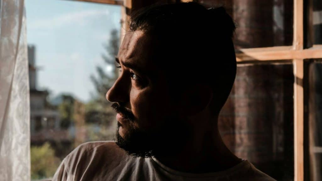 Silhouetted profile of a bearded man looking out a sunlit window.