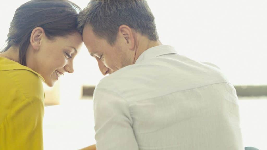 Man and woman leaning their foreheads together, the woman smiling, in a bright setting.