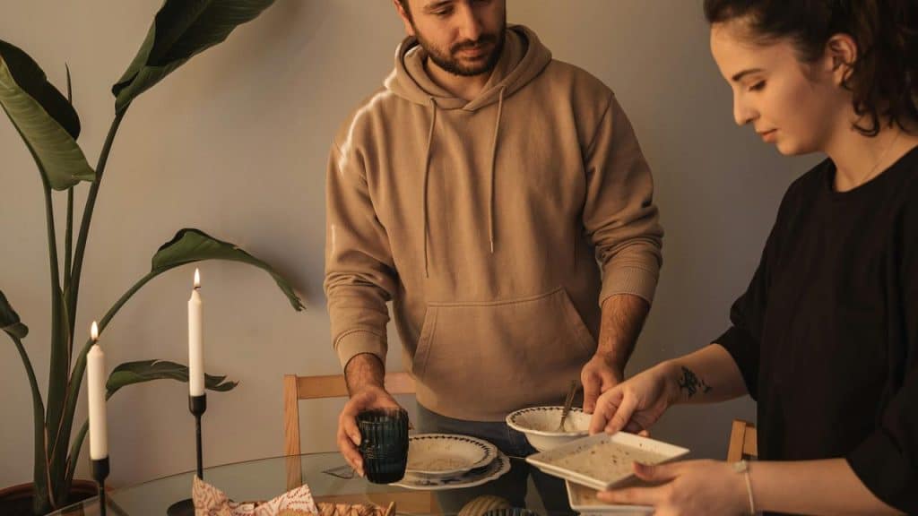 A couple clears the table after a meal in a cozy dining space.