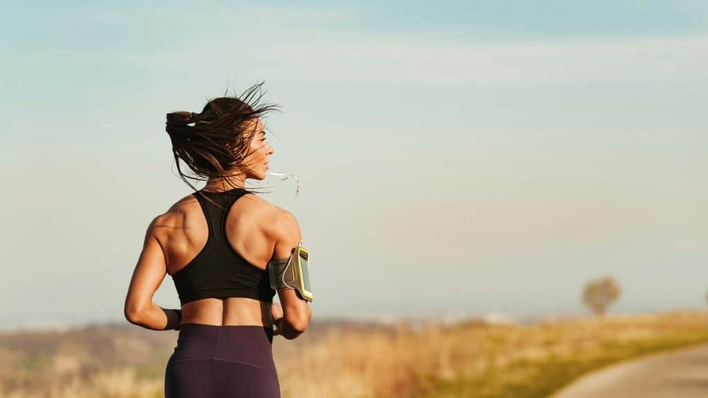 A woman jogging outdoors with earphones and an armband.