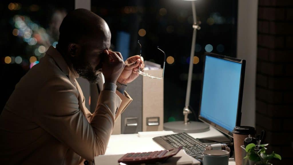 Tired man rubbing his eyes at an office desk late at night.