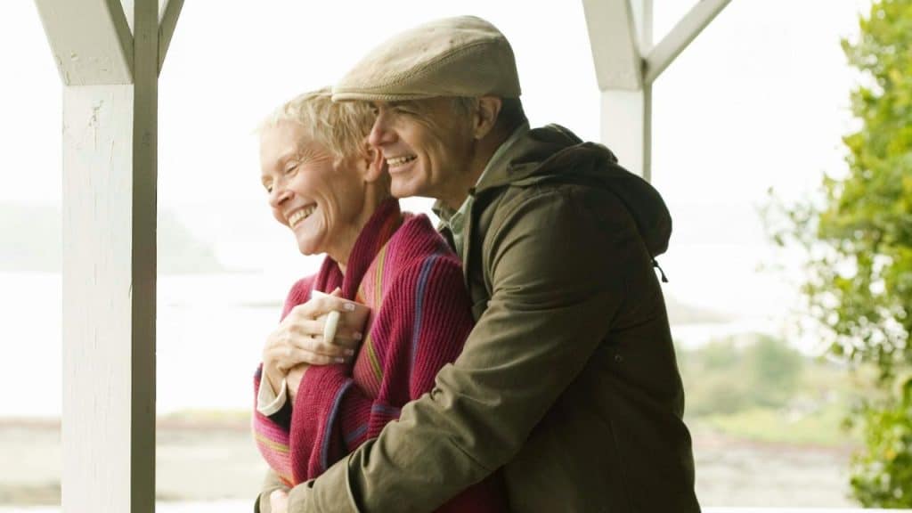 Happy older couple sitting close on a couch, smiling and touching arms.