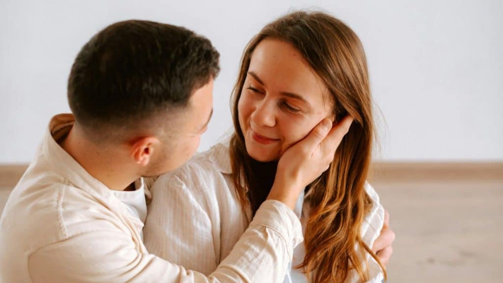 Man gently touching a smiling woman's cheek while embracing her.
