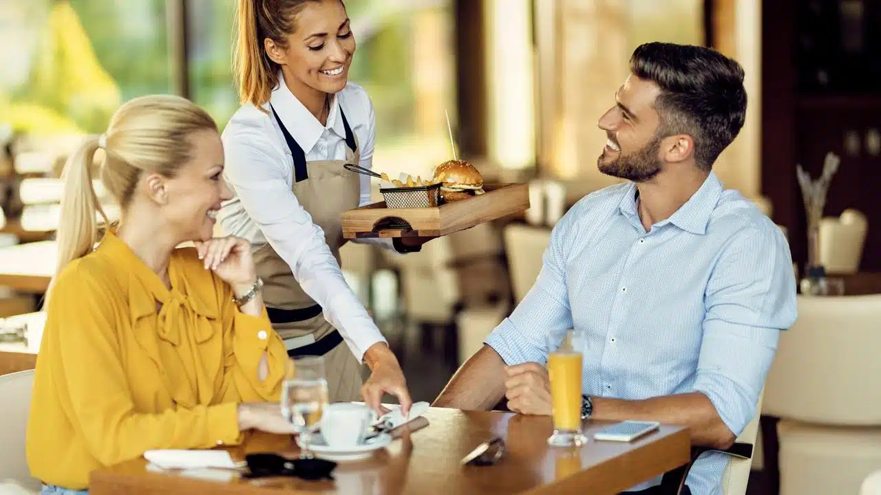 A smiling waitress serving food to a man and woman at a restaurant table.
