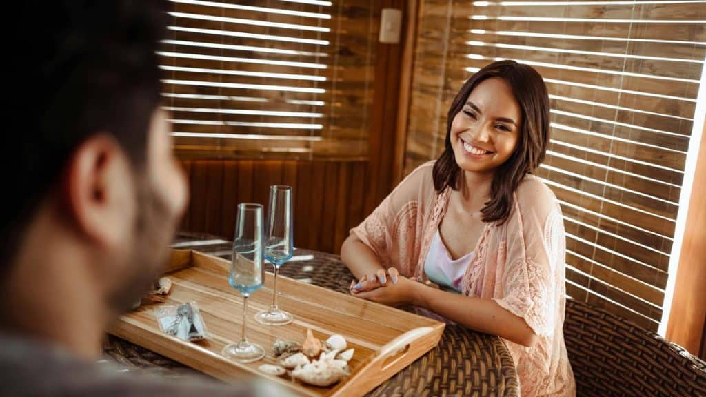 A woman smiling at a man while sitting at a table with two empty glasses.