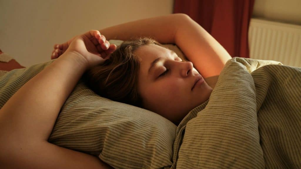 A young woman is sleeping on her back with her arms raised above her head.