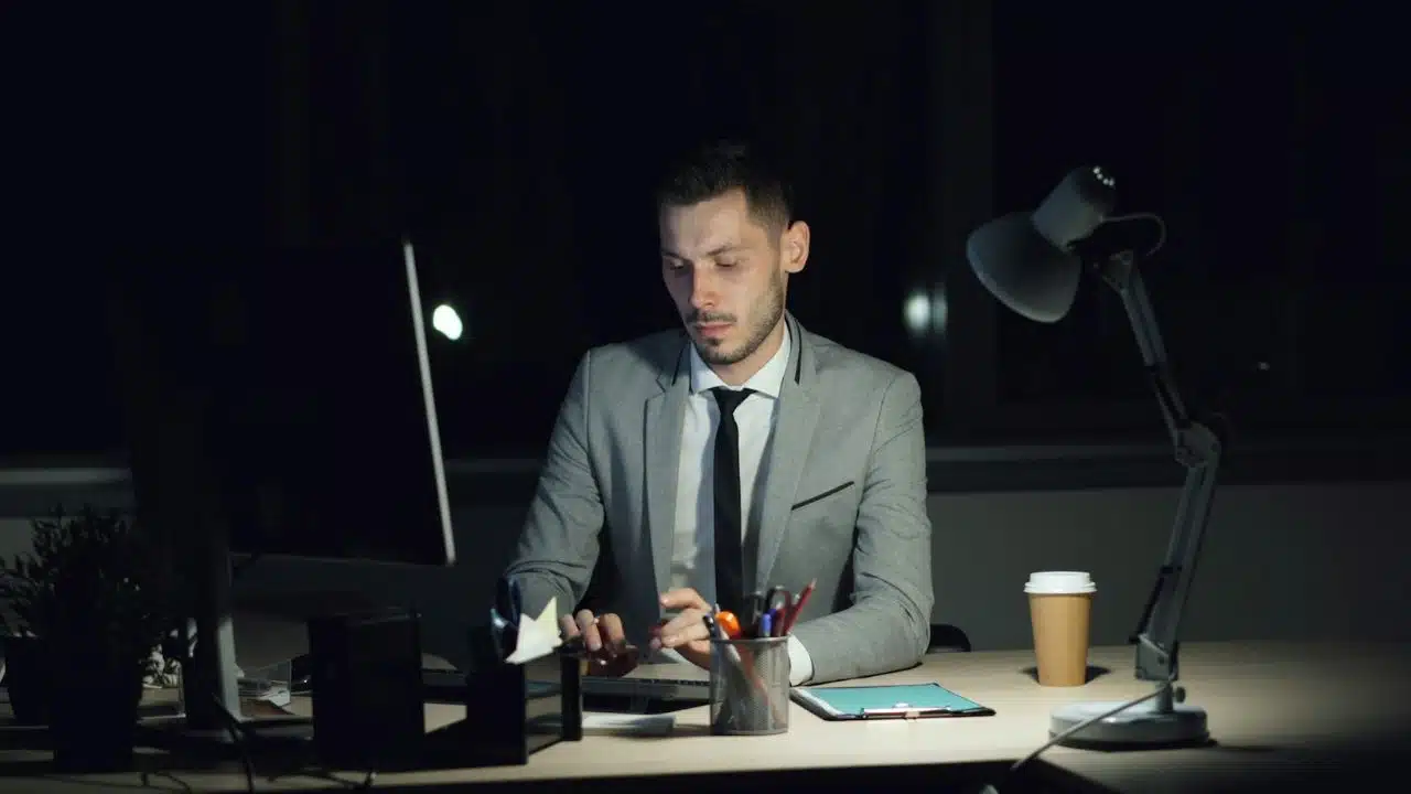 Man in a suit and tie working alone at a computer in a dark office late at night.