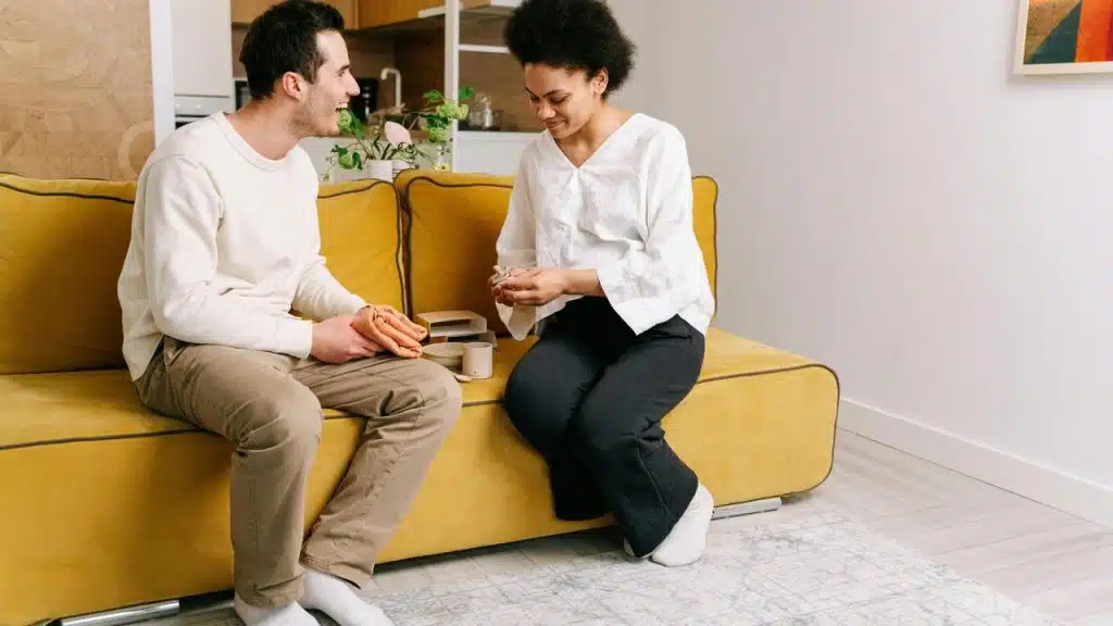 A man and woman sitting on a yellow couch and talking.