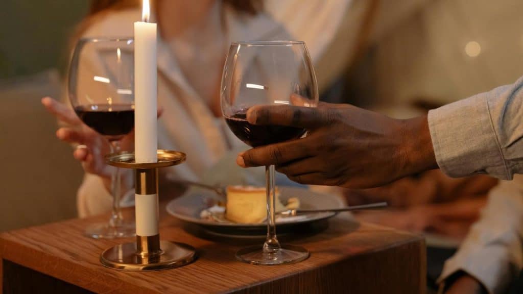 A close-up of two people clinking wine glasses beside a lit candle.