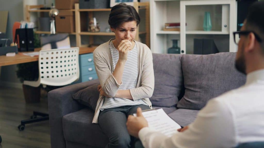 A woman sitting on a couch crying while talking to a therapist.