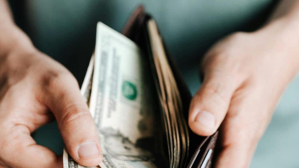 A person holding an open wallet with cash inside.