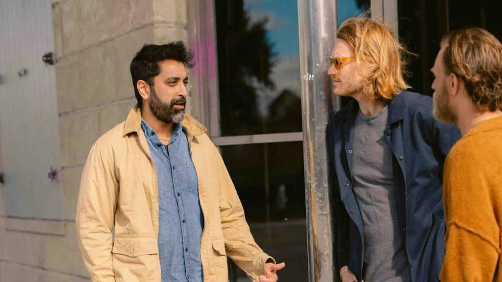 Three male friends standing outside a building and talking to each other.