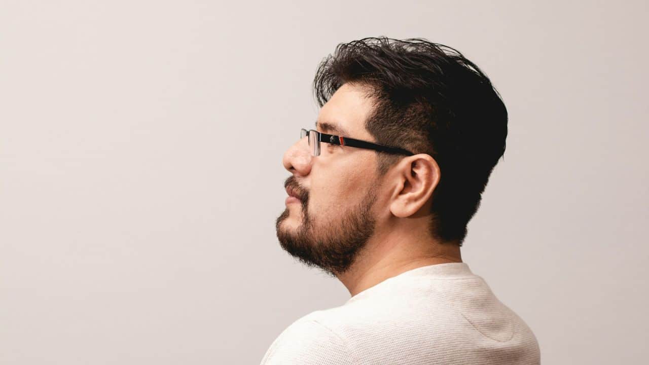 Profile view of a man with dark hair, glasses, and a short beard.