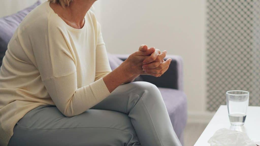 A woman sitting on a couch with her hands clasped, looking tense.