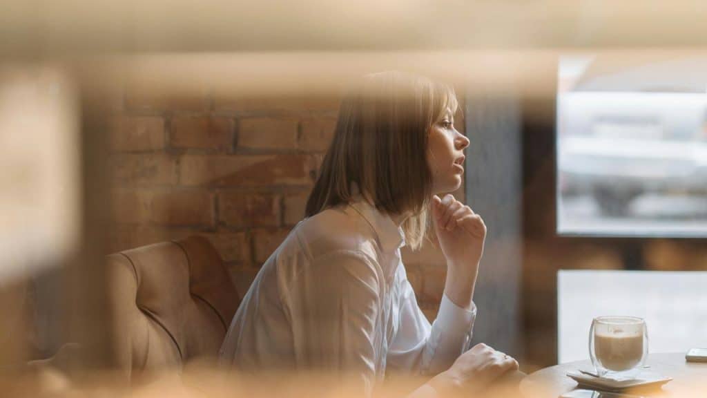 A woman sitting alone at a café table looking out the window.