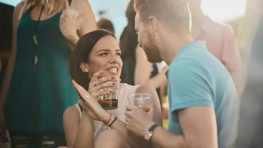 A woman and man smiling and talking while holding drinks at a social gathering.