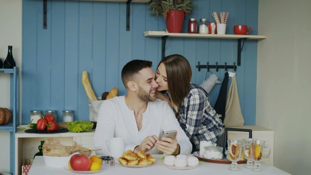A woman kissing her husband in the kitchen