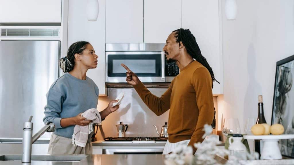 A man is pointing a finger at a woman while arguing with her in a modern kitchen.