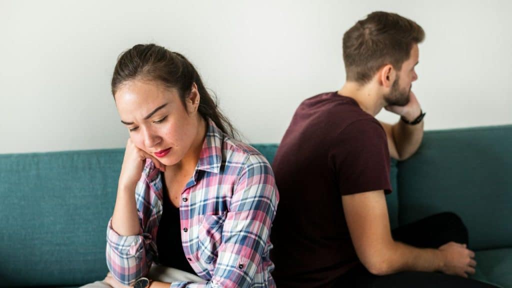 A woman looks down sadly while a man sits next to her, facing away.