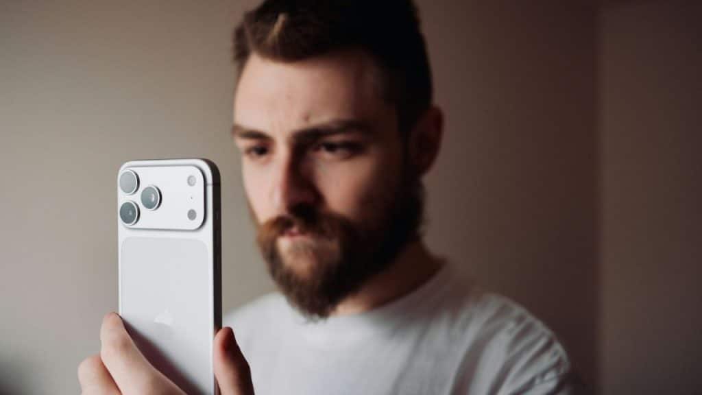 A bearded man is looking intently at the screen of a mobile phone.