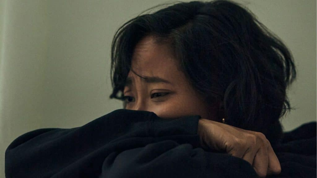 Close-up of a person with dark hair crying, covering their mouth with a sleeve.