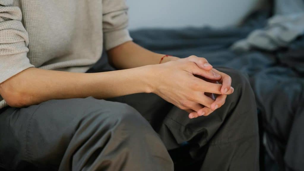 A person sitting with their hands clasped together on their lap.