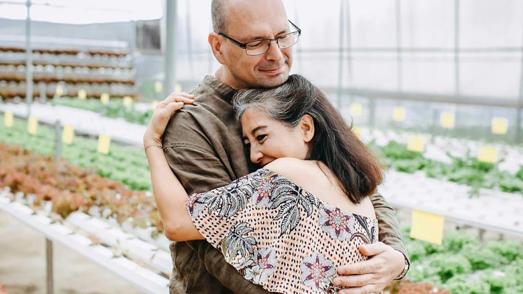 A man and woman warmly embracing in a greenhouse.