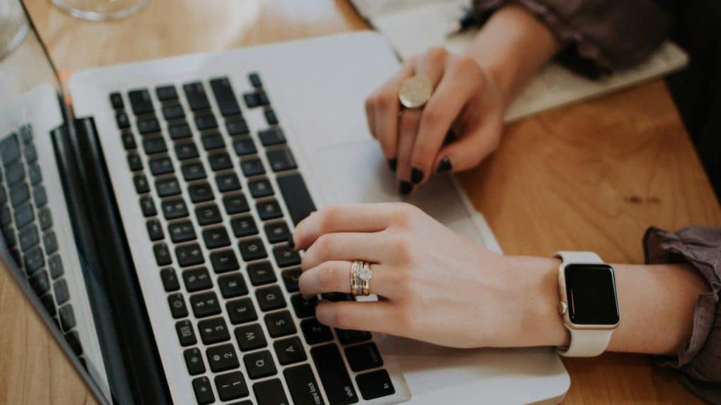 A person typing on a laptop on a wooden desk.