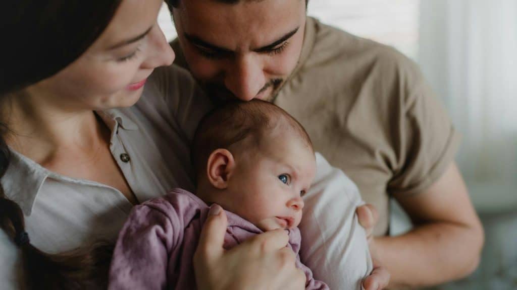 A couple holding their baby close to their arms.