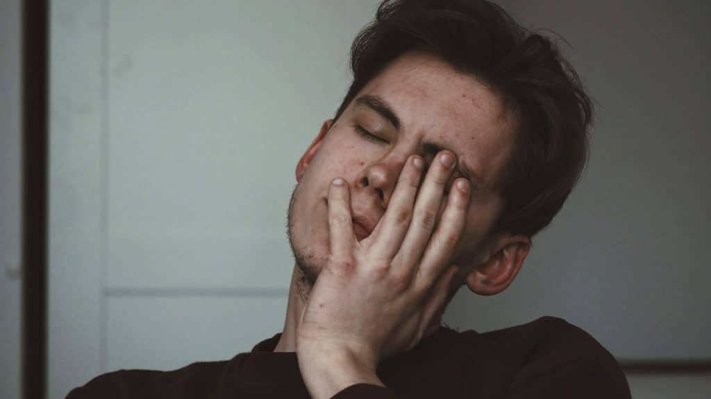A man looking tired and covering his face with his hand.