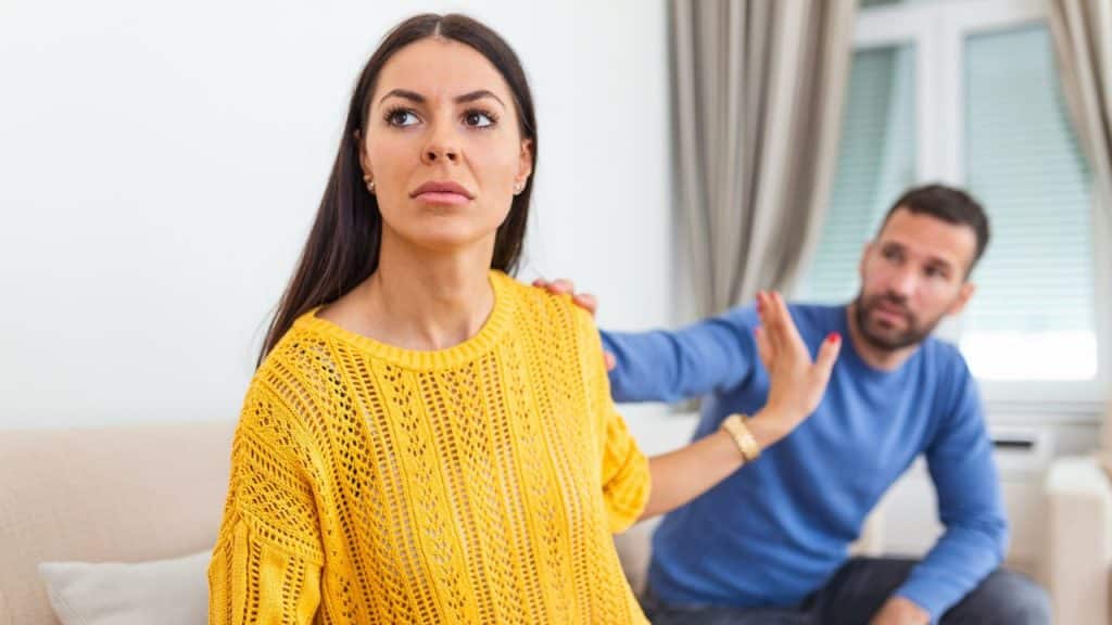 Woman in yellow sweater looking away as a man reaches out to her.