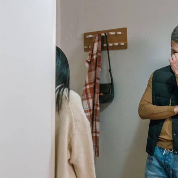 A man with a woman standing in a doorway with his hand covering his face, looking stressed or upset.