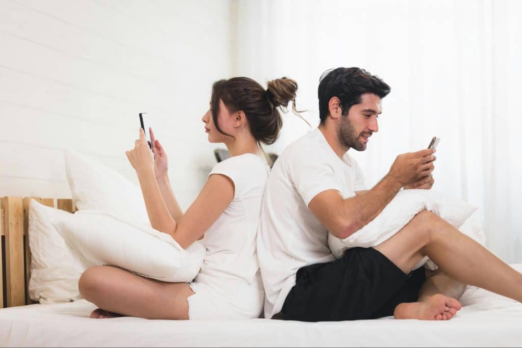 A man and woman sitting back to back and using a phone
