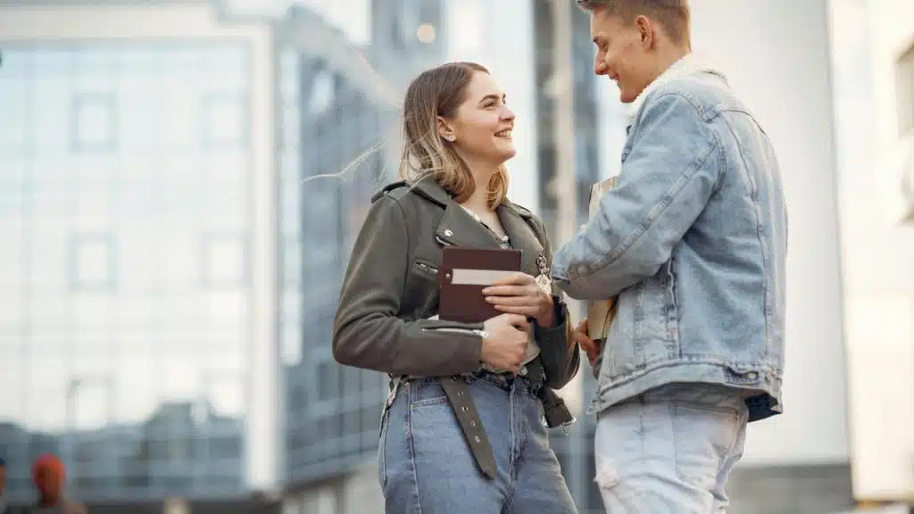 A couple smiling as they talk while holding books outdoors.