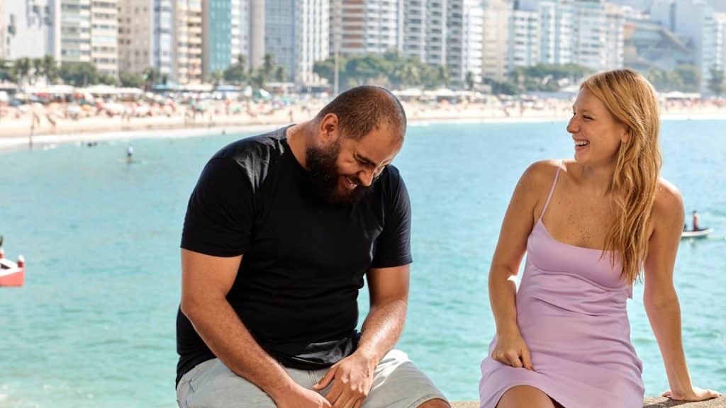 A man and a woman sitting on a wall next to the ocean.