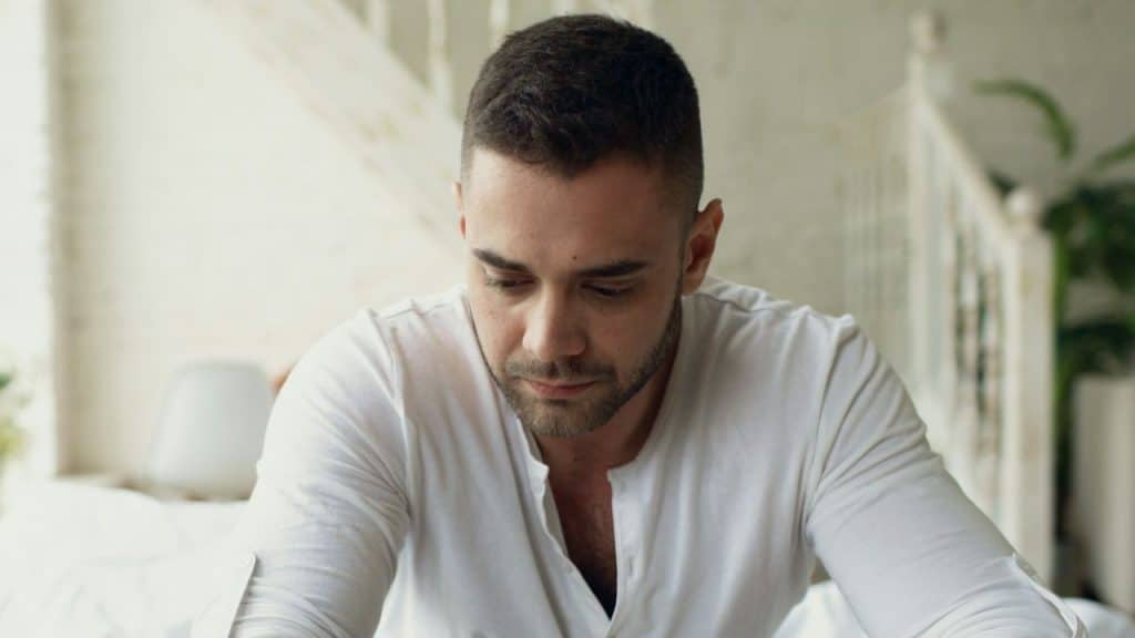 Sad-looking man in a white collared shirt seated in a brightly lit room.