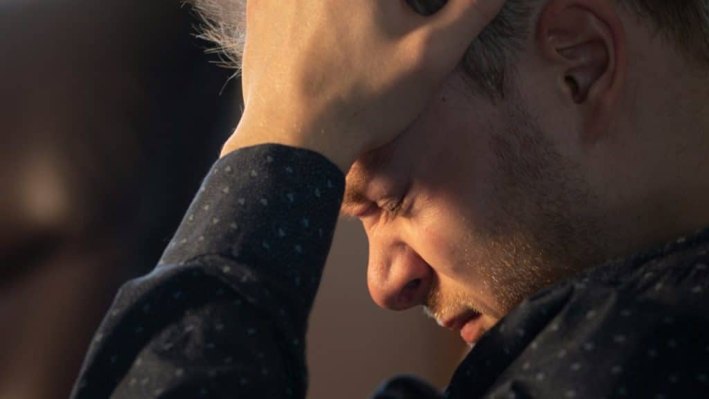 Close-up of a distressed man with his hand on his forehead, looking down.