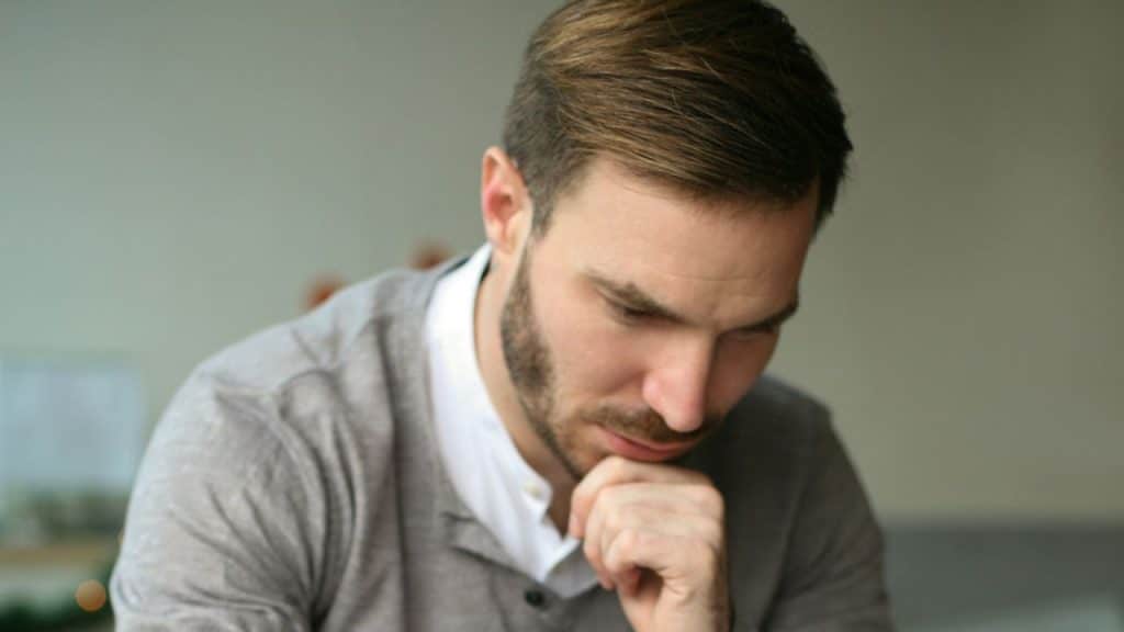 Close-up of a man with a beard, looking down, resting his chin on his hand.
