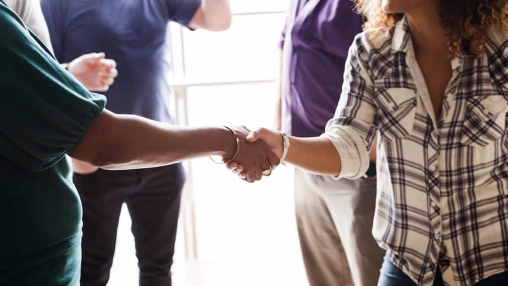 Close-up of two people shaking hands in a group setting.