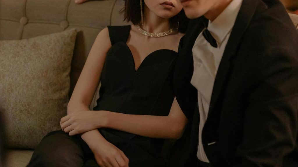 A woman in a black dress and a man in a tuxedo sitting closely together on a couch.