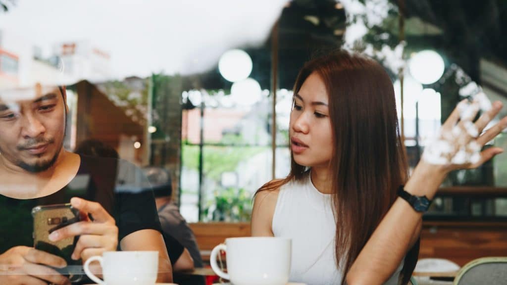 A woman is talking to her husband who is busy on his phone.