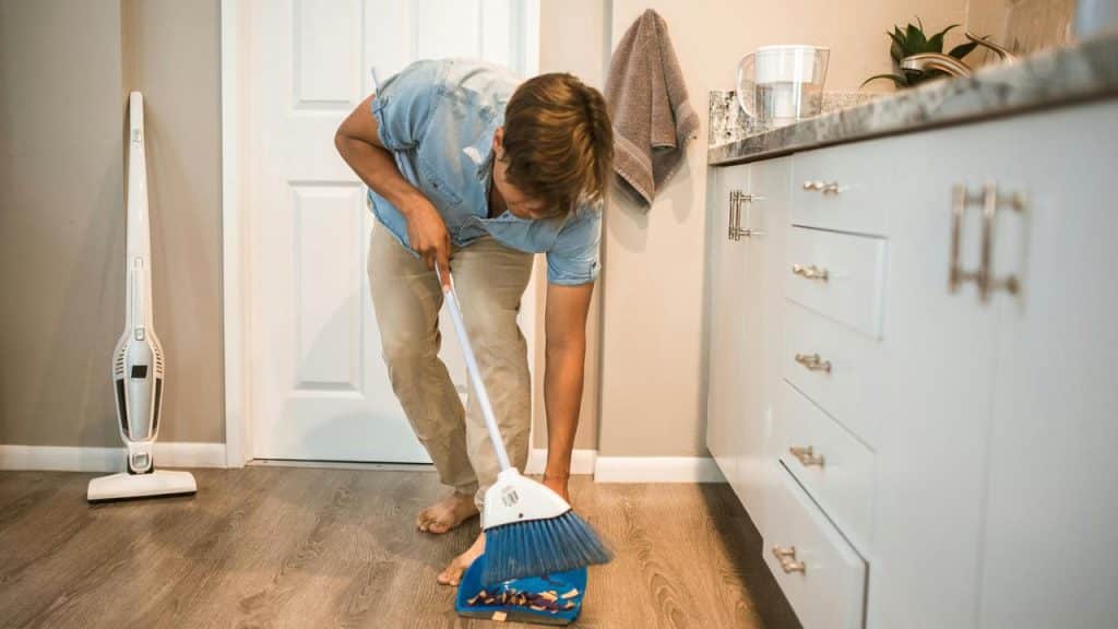 A man sweeping the kitchen floor into a dustpan.