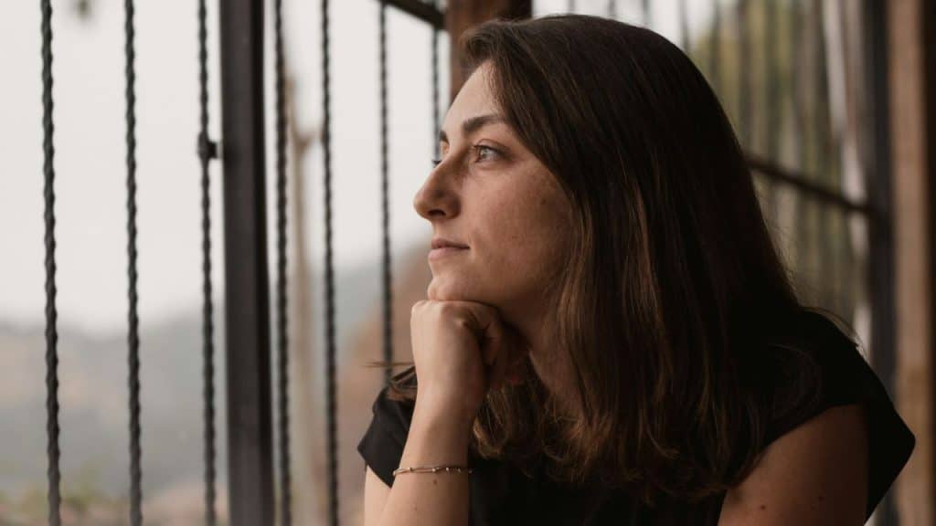 Close-up side profile of a woman looking out a window, resting her chin on her hand.
