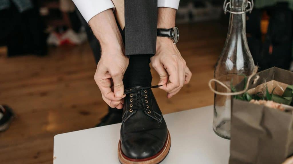 A person tying the laces of a black dress shoe.